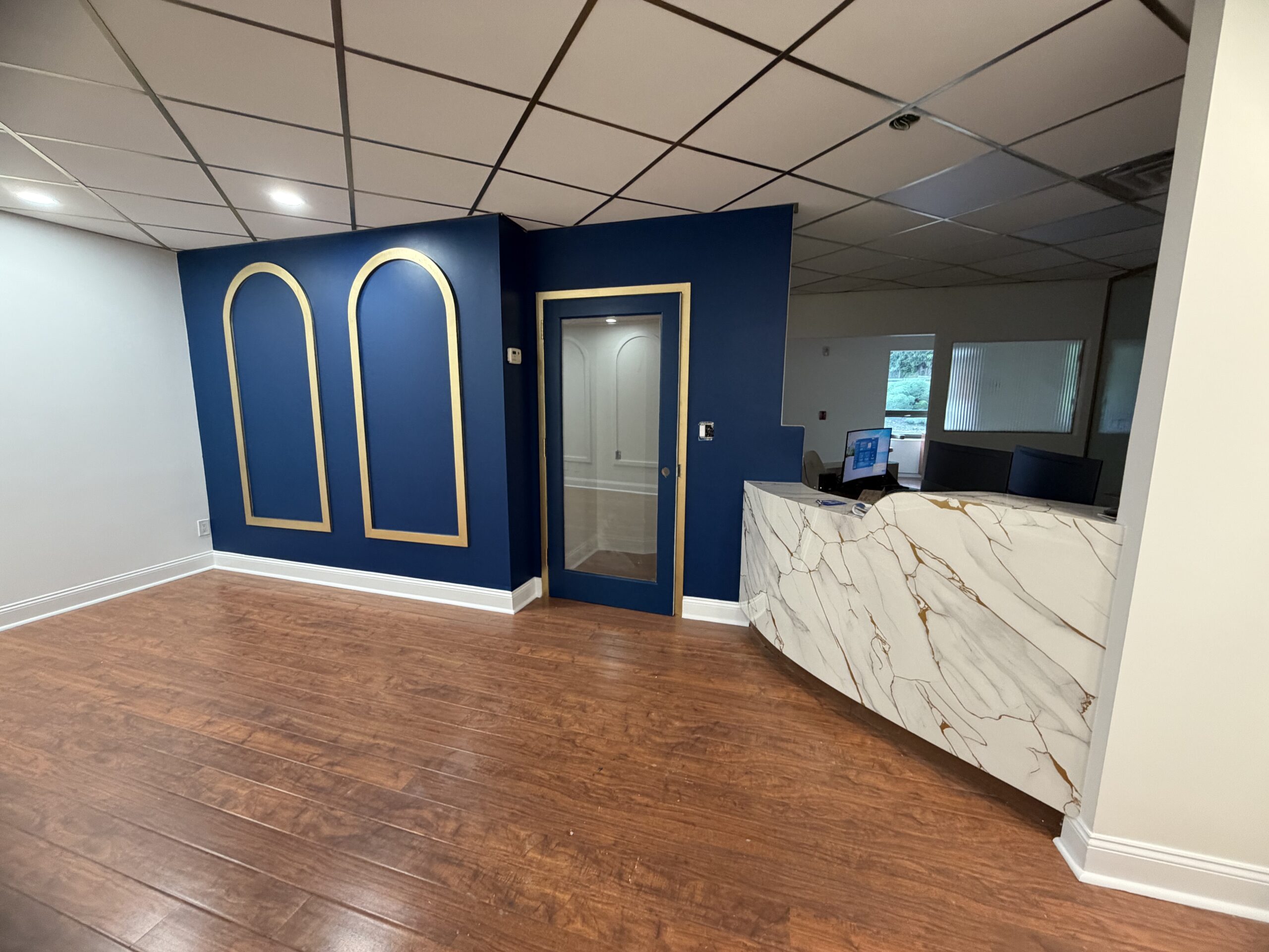Navy accent wall with gold-trimmed arched panels and a glass consultation door in a dental practice