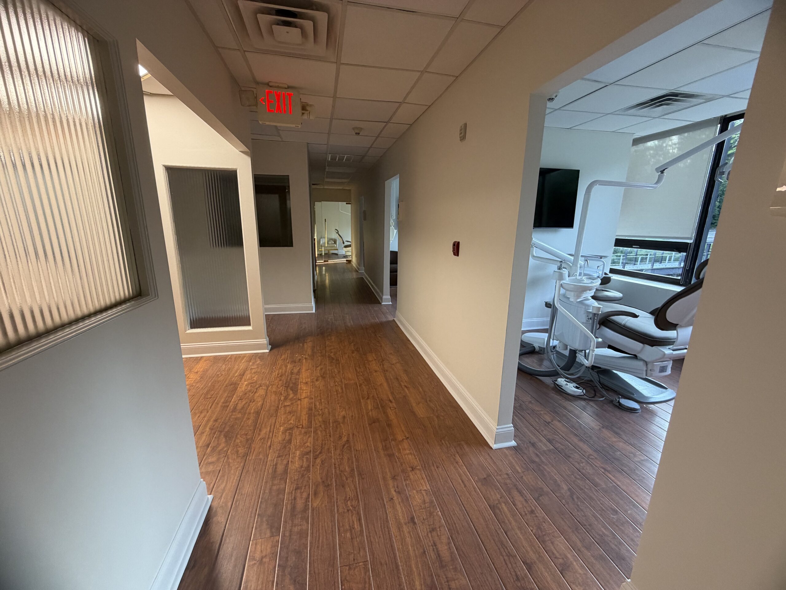 Dental office hallway with wood-look flooring and fluted glass operatory entries